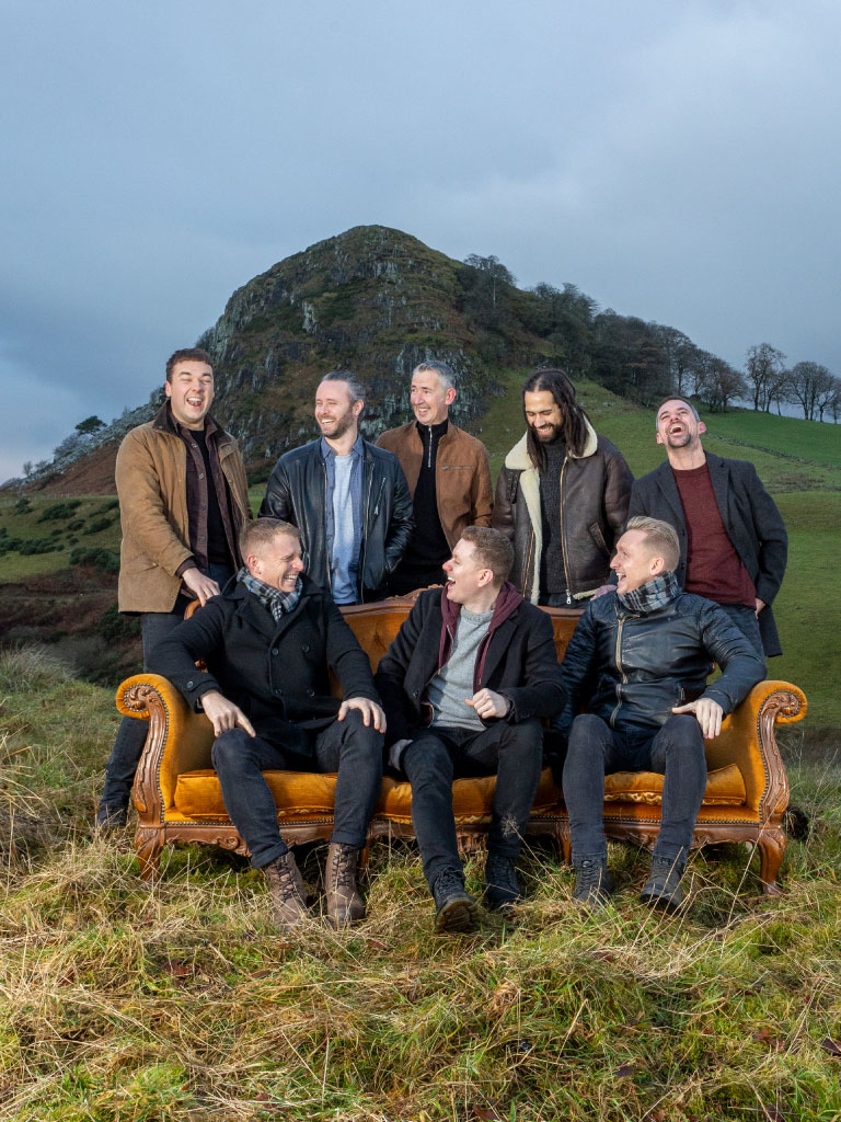 the members of the band skerryvore pose by a couch outside with a view of scottish highlands behind them