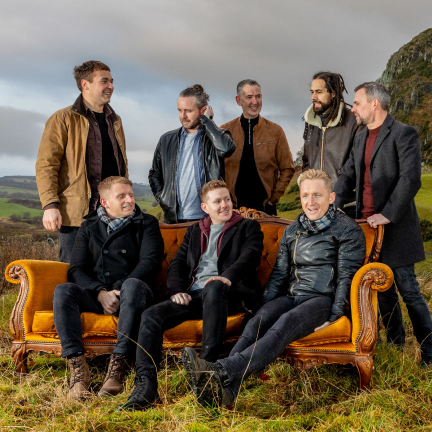 the members of the band skerryvore pose by a couch outside with a view of scottish highlands behind them