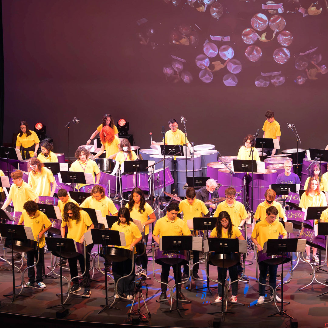 A large group of students plays steel band drums on the stage